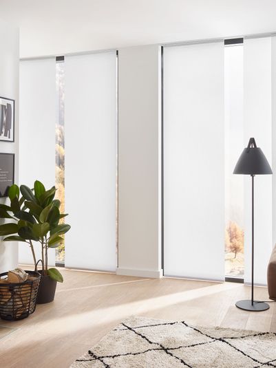 Moderne Wohnzimmereinrichtung mit einem Kamin, einer Stehlampe, einem Sofa und Pflanzen. Helle, lichtdurchlässige Vorhänge lassen Tageslicht herein.