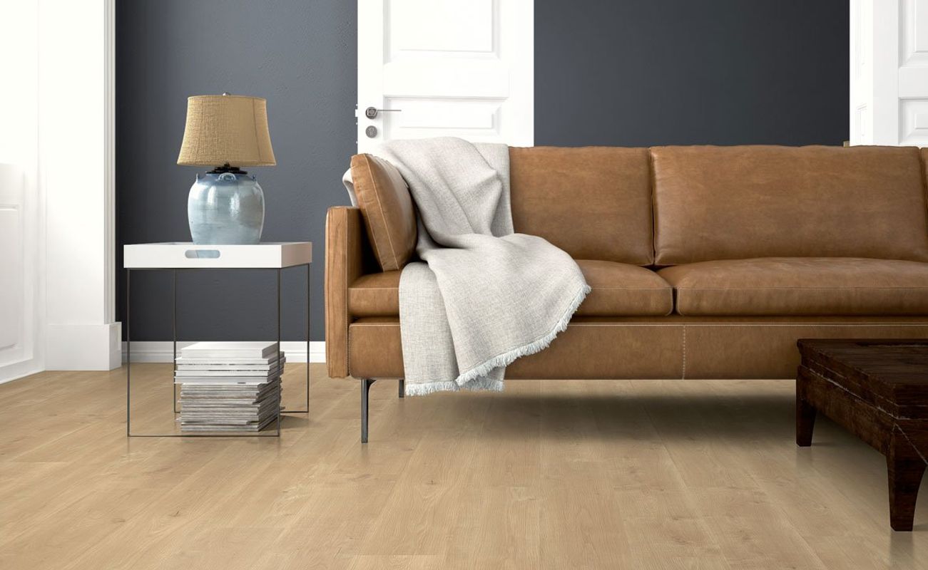 Ein Wohnzimmer mit einem braunen Ledersofa, einem Tisch mit einer Lampe und einem Beistelltisch. Der Boden ist hell und die Wände sind dunkel.